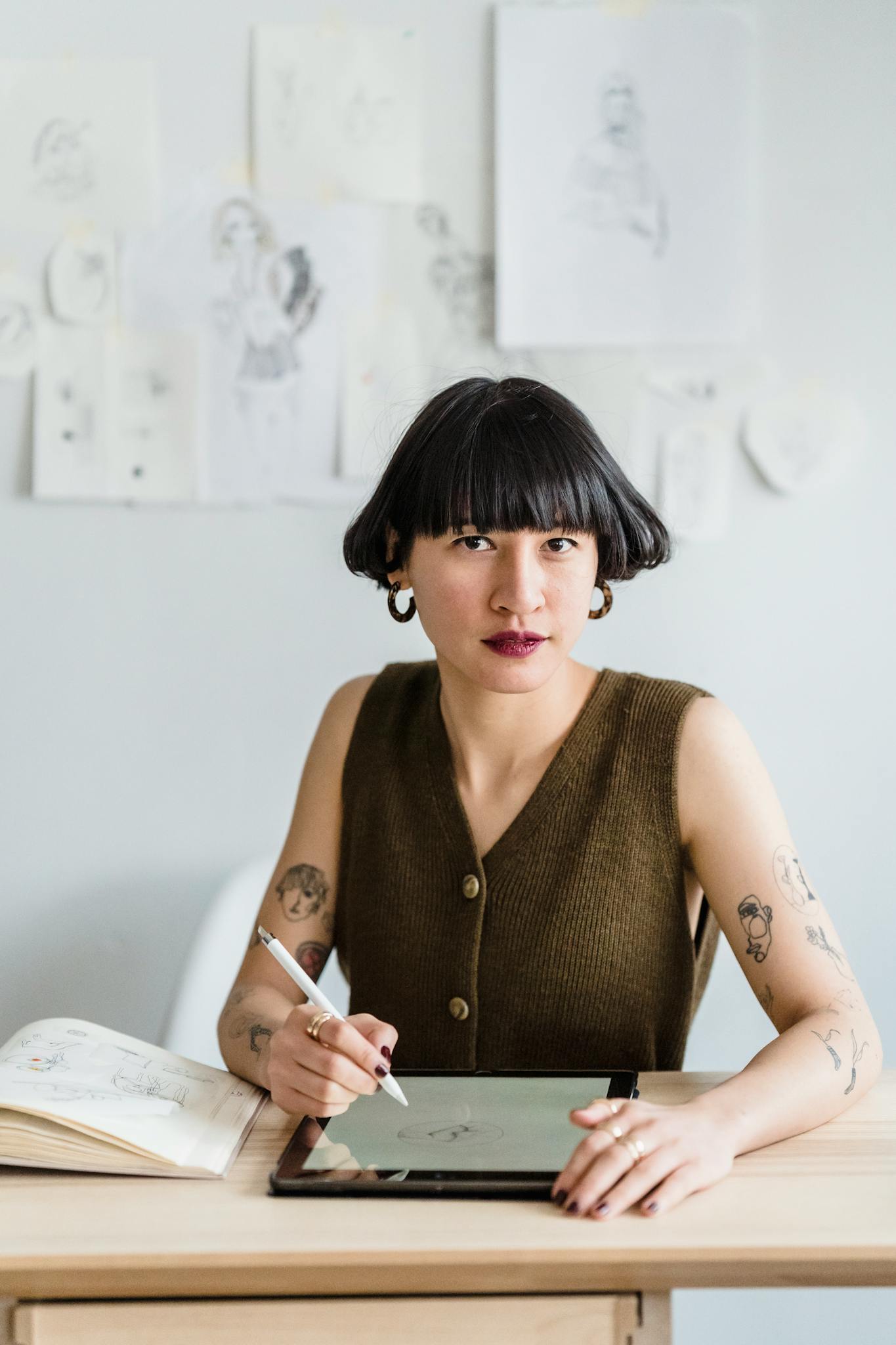 Asian female looking at camera while sitting at table and drawing in graphics tablet